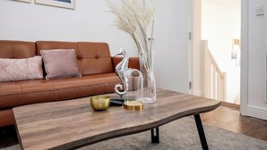 A living room with a brown leather sofa, a wooden coffee table with decorative items, and a clear glass vase with pampas grass. - Beautiful Flat Near the Center 11 min  (London)