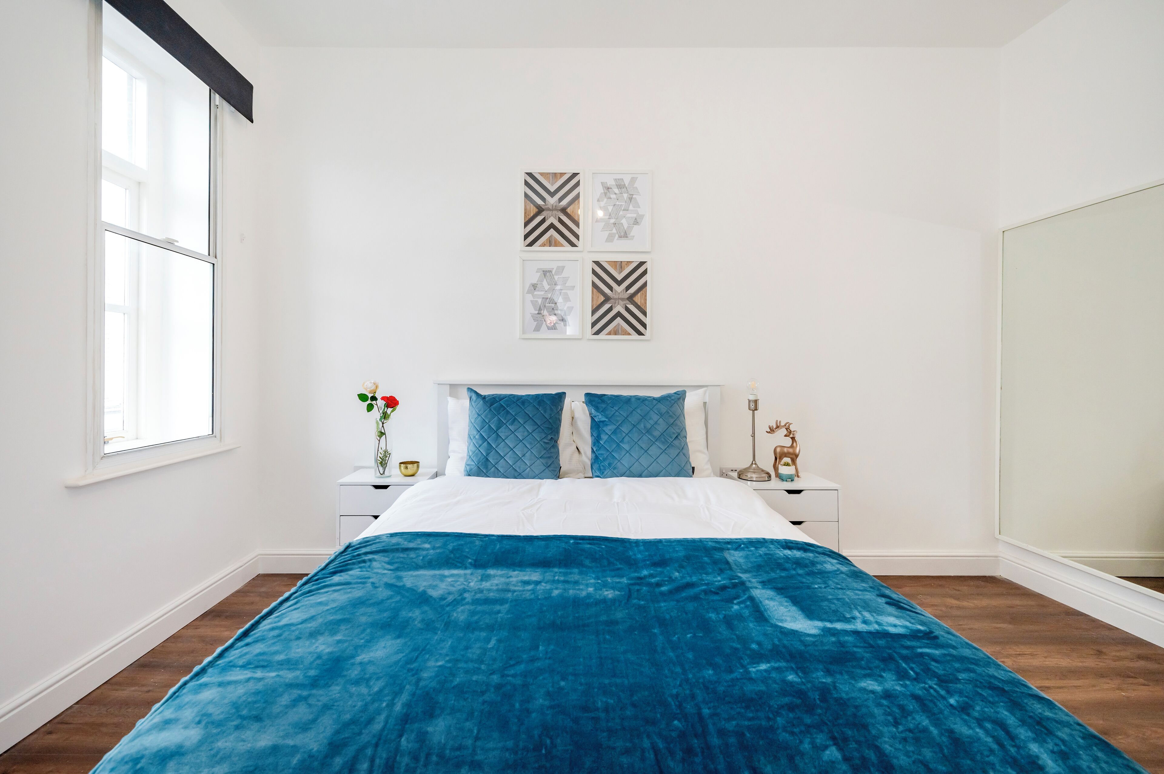 A bedroom with a bed, white walls, a window, and a nightstand with a vase and a lamp.