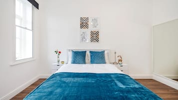 A bedroom with a bed, white walls, a window, and a nightstand with a vase and a lamp.