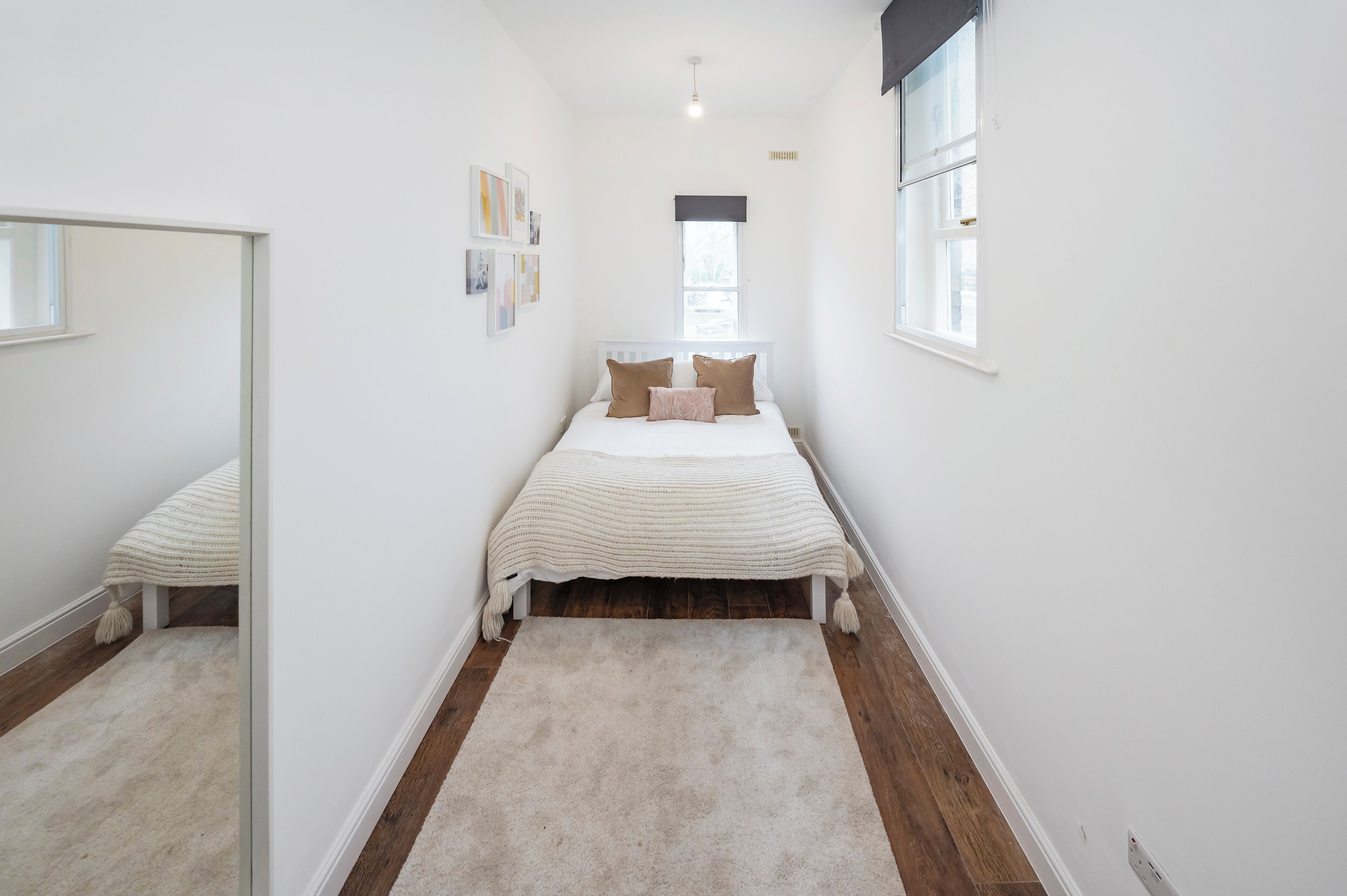 A narrow bedroom with a single bed, a large mirror, and a window.