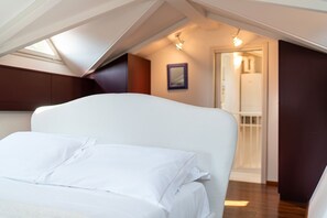 Ein Schlafzimmer mit einem weißen Bett, einer geneigten Decke und einer Tür zu einem Badezimmer.