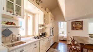 Une cuisine spacieuse avec des meubles blancs, une grande fenêtre et un coin repas comprenant une table et des chaises en bois.