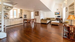 Un vaste espace de vie doté d’un plancher en bois, d’une table à manger avec des chaises, d’un canapé, d’une télévision et d’une lampe.