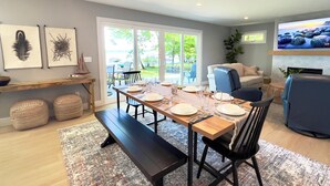 A dining area with a wooden table set for four, benches, and a view of the outdoors through large sliding doors. - Green Lake Getaway Lakefront Hot Tub Kayak SUP (Interlochen)