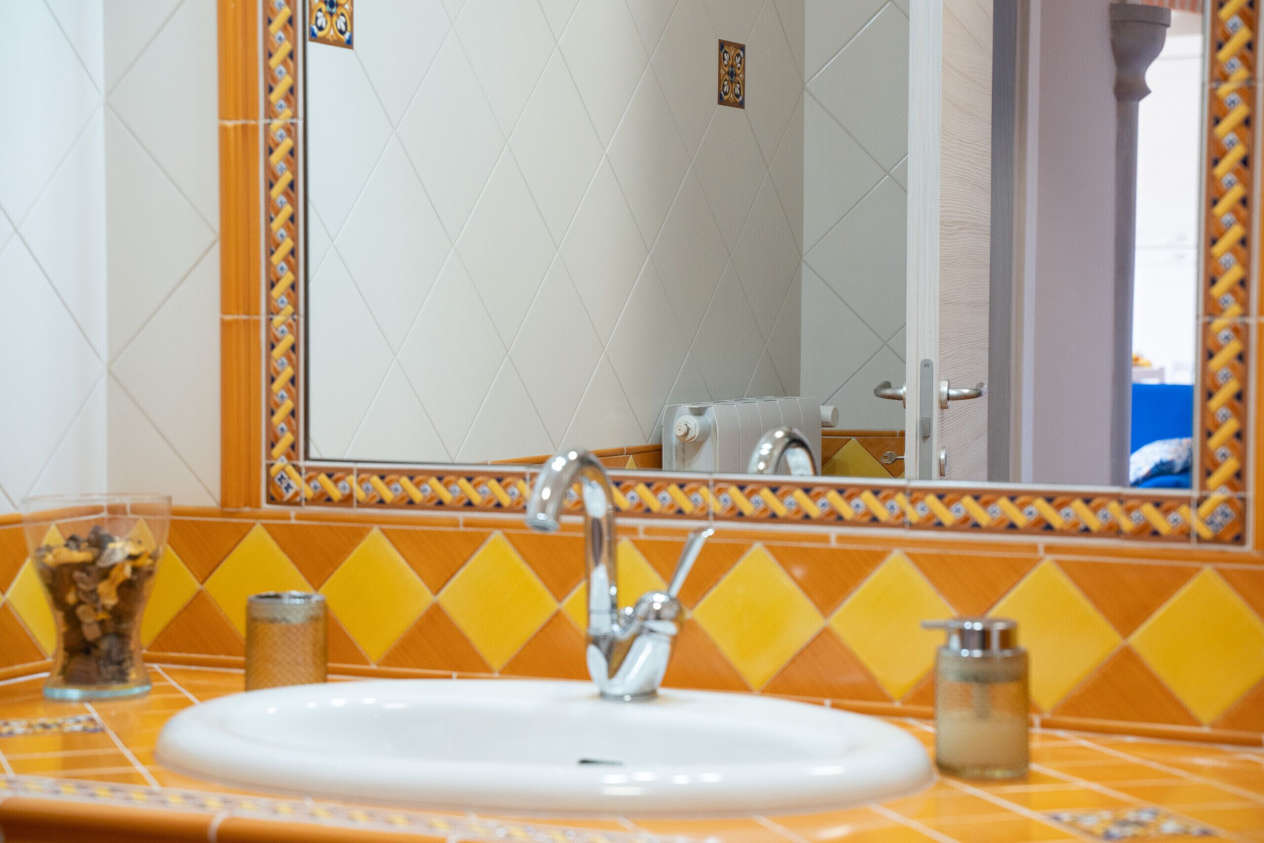 Un bagno con un lavandino bianco, uno specchio e una parete piastrellata con motivo a rombo giallo.