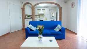 A living room with a blue sofa, a white coffee table with a vase, and a kitchen in the background. - Casa Francese Relax - An oasis of well-being not far from the sea (Tramonti)