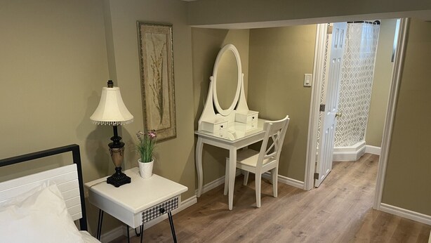 A bedroom with a bed, a bedside table with a lamp, a desk with a mirror, and a chair.