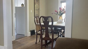 A living room with a brown sofa, wooden dining table, and chairs. There is a ceiling fan above the table.