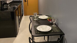 A compact kitchen with a dining area, featuring a microwave, stove, and a small table set for two with plates and glasses.