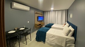 A hotel room with two beds, a TV, a desk with chairs, and an air conditioning unit.