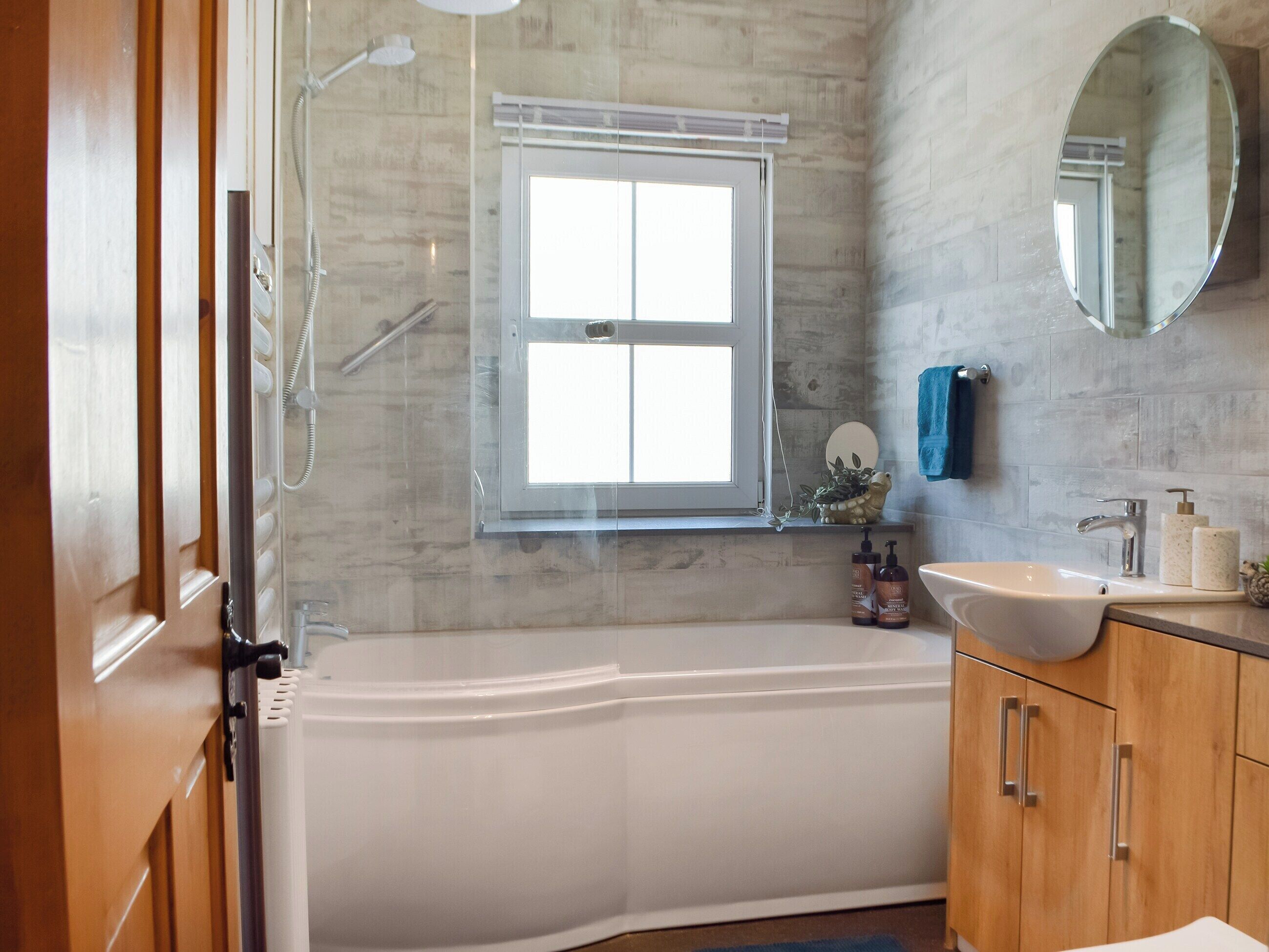A bathroom with a bathtub, a window, a mirror, and wooden cabinets.