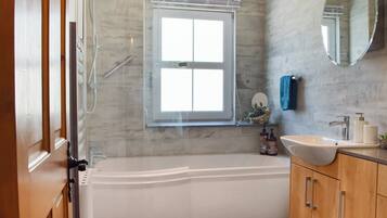 A bathroom with a bathtub, a window, a mirror, and wooden cabinets.