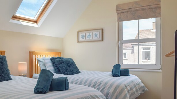 A bedroom with two beds, a skylight, a window, and a framed picture on the wall.