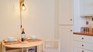 A small dining area with a round table, two white bowls, a wine bottle, and a candle. There is a white chair and a cabinet with drawers.