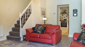 A living room with a red leather sofa, a staircase, a chandelier, and a kitchen in the background.