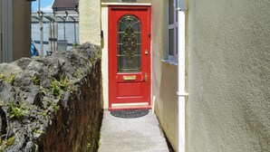 A narrow alleyway with a red door, a small window, and a mailbox on the wall.