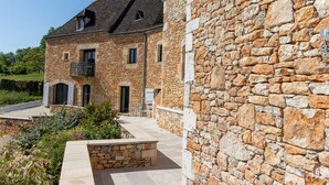 A stone building with a sloped roof, a small balcony, and a paved courtyard. - Holiday Home 'Gite Les Hauts De L'ouysse' with Private Pool, Wi-Fi and Air Conditioning (Lacave)