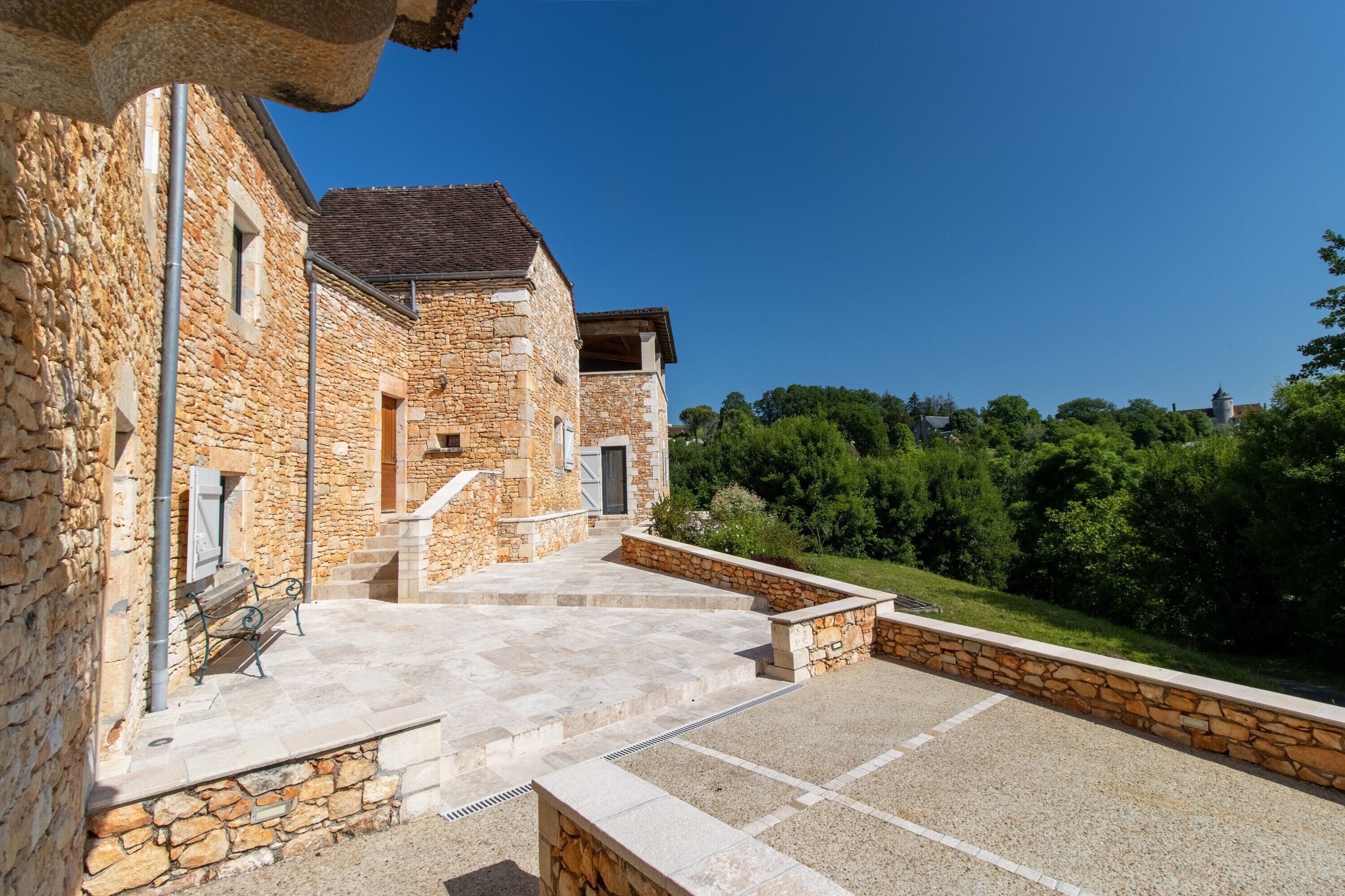 Un bâtiment en pierre doté d’une cour, d’un escalier menant à une porte et d’un banc.