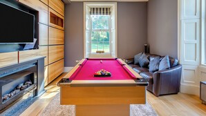 A pool table in a room with a television on the left, a sofa with cushions, and a window with blinds. - 6 bedroom accommodation in Old Quarrington, near Durham (Old Quarrington, near Durham)
