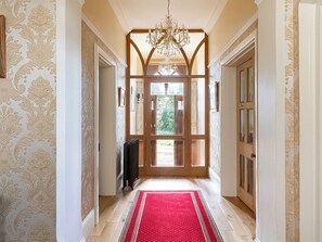 A hallway with patterned wallpaper, a red carpet, and a wooden door leading outside.
