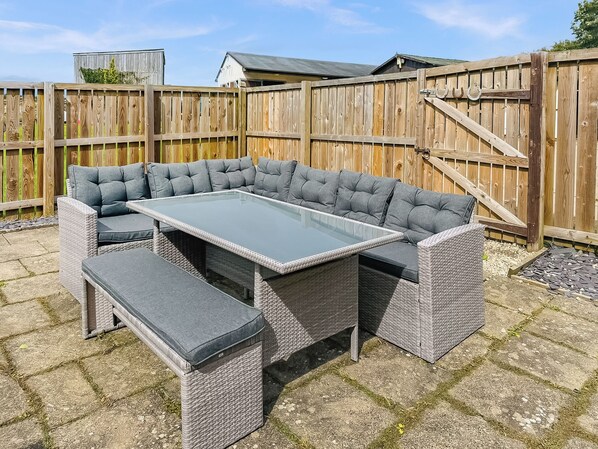 A corner sectional sofa with a glass-top table and matching ottoman in a backyard setting.