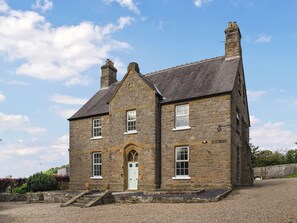 A stone building with a central entrance, two chimneys, and a gravel driveway.