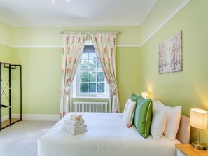 A bedroom with a bed, a radiator, a window with floral curtains, a bedside table with a lamp, and a wall with a painting. - 6 bedroom accommodation in Old Quarrington, near Durham (Old Quarrington, near Durham)