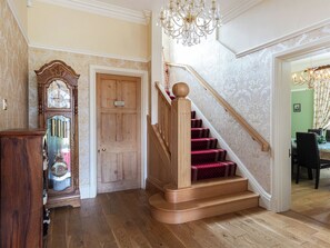 Un magnifique escalier, avec des marches recouvertes de moquette rouge et une rampe en bois, menant à une salle à manger.