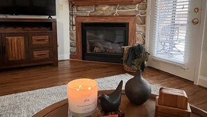 A living room with a stone fireplace, a television, and a book on a coffee table. - WALK to City Center! Elevator & 2 BDRMS just off Main St. (Helen)