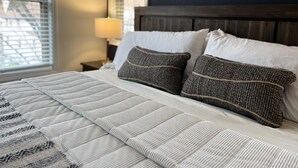 A neatly made bed with a striped blanket and two textured pillows, a wooden headboard, and a wall-mounted artwork above it. - WALK to City Center! Elevator & 2 BDRMS just off Main St. (Helen)