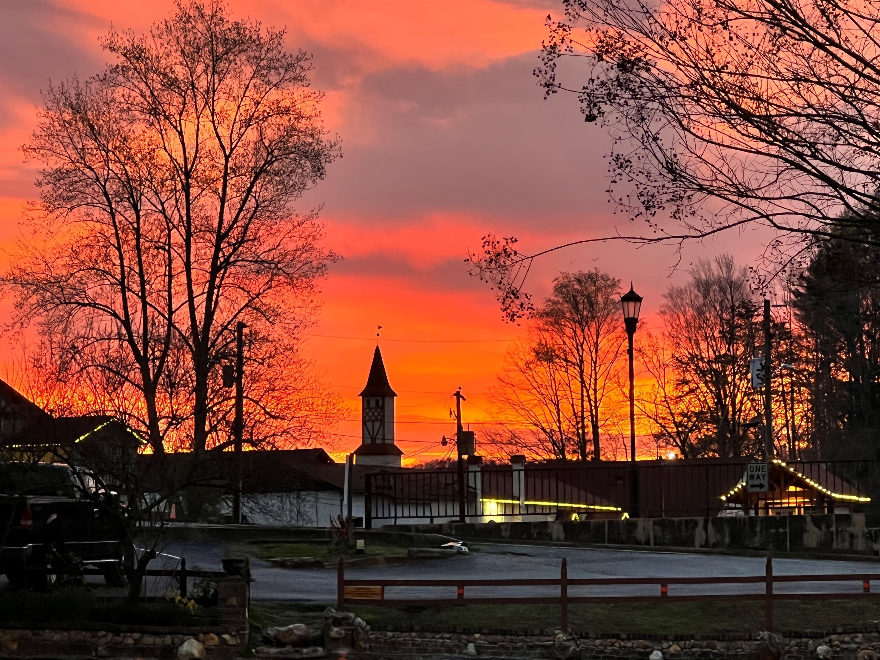 Un atardecer sobre un pueblo con una imponente torre del reloj, una farola y una valla.