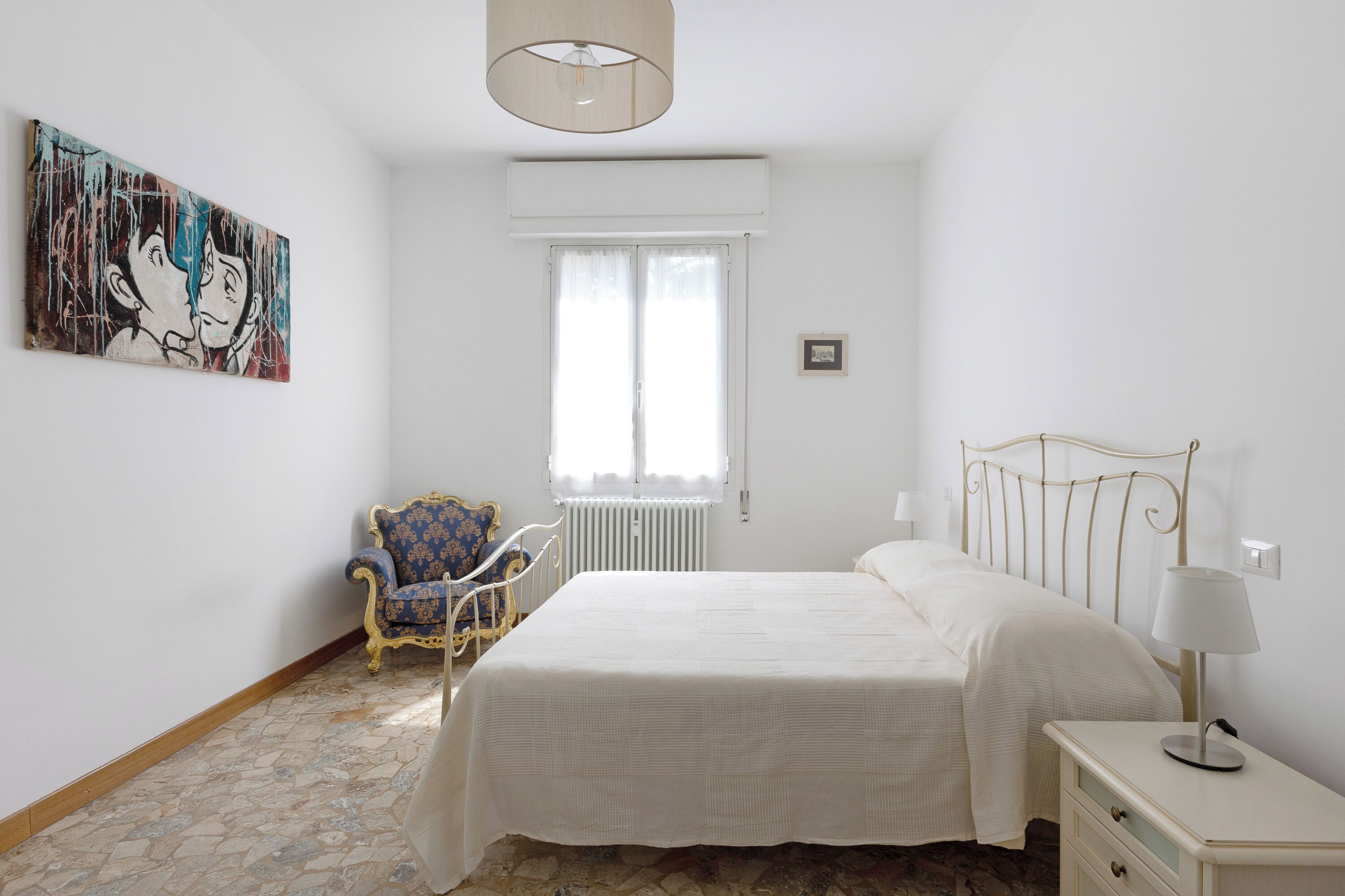 Una camera da letto con un letto, una sedia, una lampada e un quadro appeso al muro.