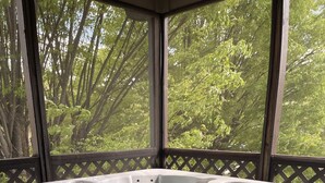 A hot tub with a wooden deck and a view of trees.