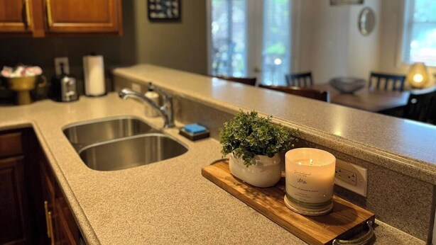A kitchen with a granite countertop, stainless steel sink, wooden cabinets, a potted plant, and a candle.