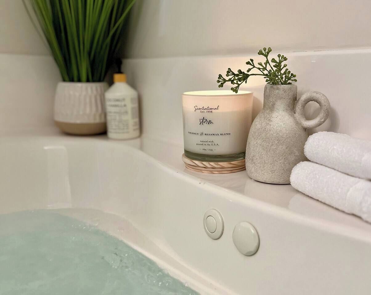 A bathtub with a candle and a plant on the edge.