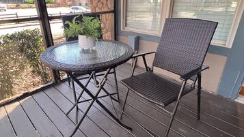 Ein runder Glastisch mit einem Stuhl aus Metall auf einer Holzdielen-Terrasse.