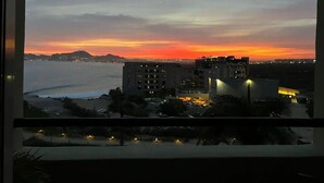 Une vue sur le coucher de soleil, prise depuis une fenêtre donnant sur une zone côtière avec des bâtiments et une étendue d’eau.