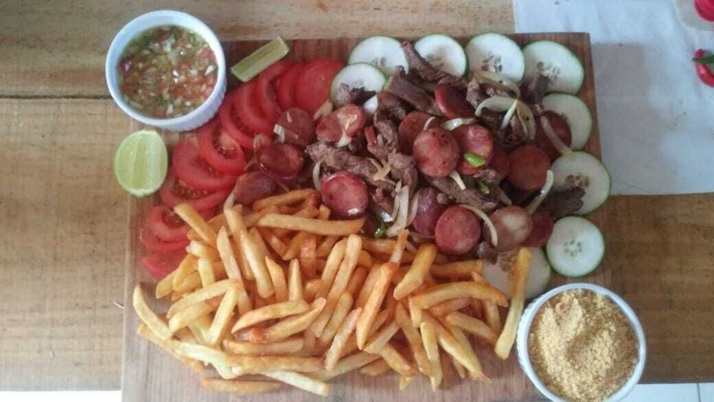A wooden table with a variety of food items including sliced tomatoes, onions, meat, and French fries, along with small bowls of condiments.