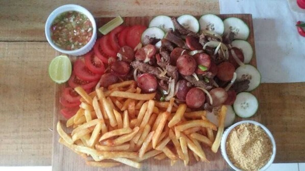A wooden table with a variety of food items including sliced tomatoes, onions, meat, and French fries, along with small bowls of condiments. - Pousada e Balneário Recanto dos Passaros BRB (Barreirinhas)