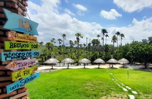 A pathway leading to a pool area with palm trees and thatched umbrellas. - Pousada e Balneário Recanto dos Passaros BRB (Barreirinhas)