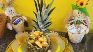 Un plateau de fruits comprenant un ananas, des oranges et un panier de maïs.