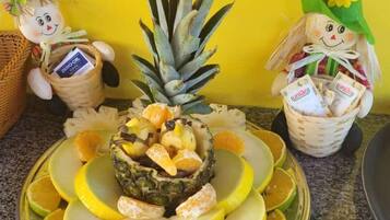 Uma tábua de frutas com abacaxi, laranjas e uma cesta de milho.
