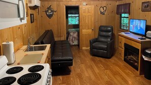 Un interior de cabaña acogedor con kitchenette, sofá, chimenea y televisor.