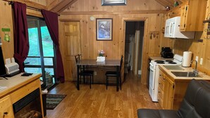 Una habitación acogedora estilo cabaña, con interior de madera, una mesa de comedor con sillas, una kitchenette y una chimenea.