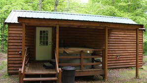 Una cabaña de troncos con una terraza de madera, un banco y un cubo de basura.