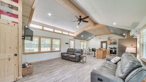 A spacious living area with a gray leather sofa, a wooden ceiling, and a kitchen in the background. - Secluded Broken Bow Cabin w/ Fishing Pond & Views! (Broken Bow)