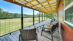 A covered outdoor deck with wicker furniture and a view of a grassy field. - Secluded Broken Bow Cabin w/ Fishing Pond & Views! (Broken Bow)