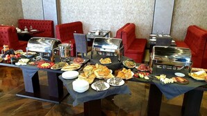 Un buffet proposant une variété de plats et de couverts disposés sur des tables, entouré de sièges rembourrés de tissu rouge.