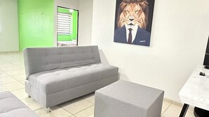Una sala de estar moderna con un sofá gris, un reposapiés a juego y un ventilador de techo. En la pared, un cuadro grande con un león.