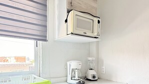 Una kitchenette pequeña con microondas, cafetera y licuadora sobre la encimera.